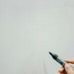 Close-up of hand holding black marker, ready to write on whiteboard.