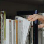 Close-up of a hand picking a book from a library shelf, symbolizing knowledge and education.
